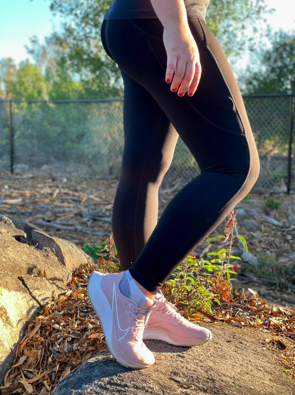 Close up shot of a woman wearing black leggings and pink sneakers while standing on a rock