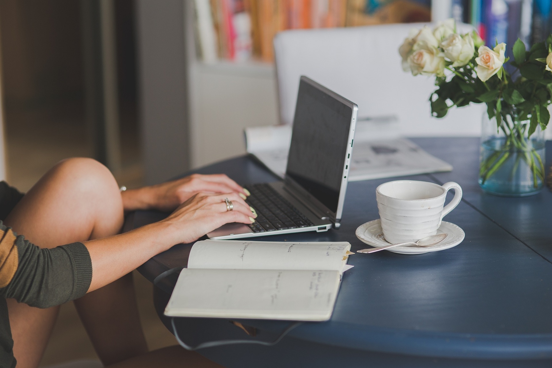 Woman typing on her laptop while her notebook is open on the table