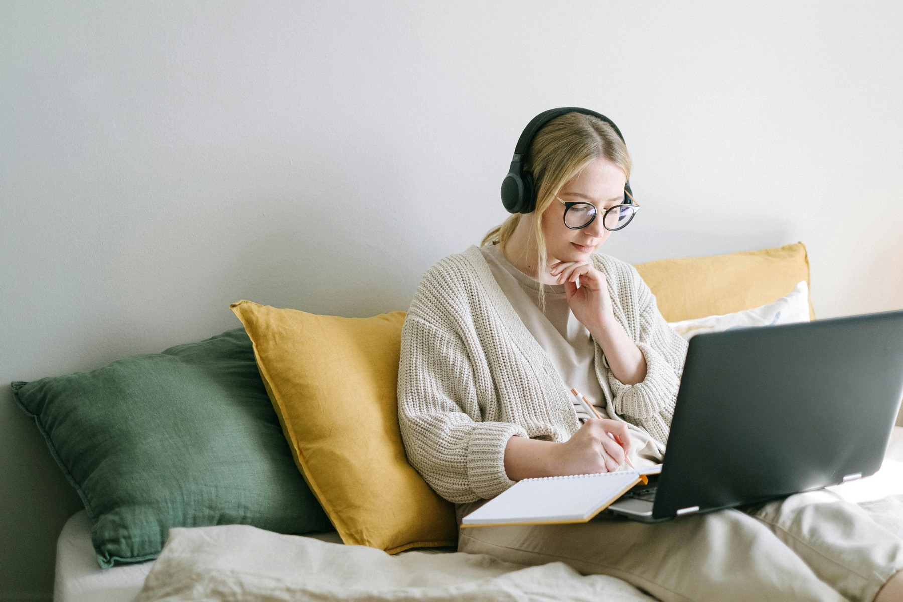 Woman wearing headphones while writing on her notebook while using her laptop
