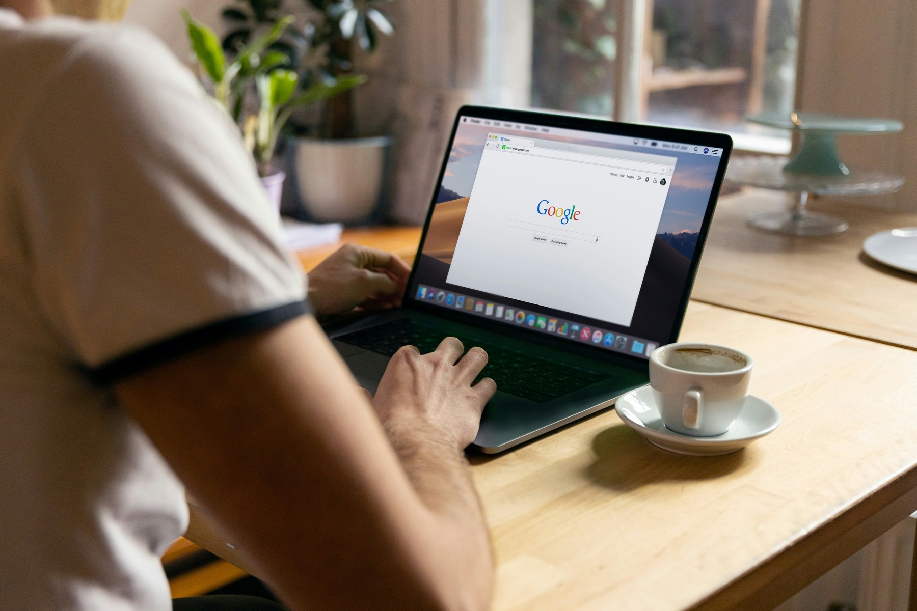 Person using a laptop with the Google homepage open, sitting at a table with a cup of coffee beside them.